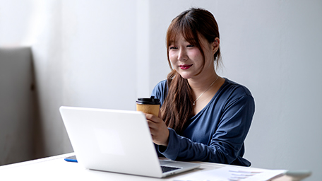 Woman holding coffee cup on laptop registering for portal