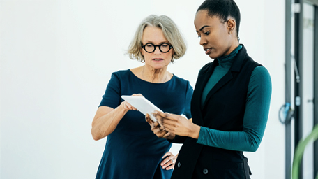 Two female business professionals standing in office using digital tablet discussing about new project.