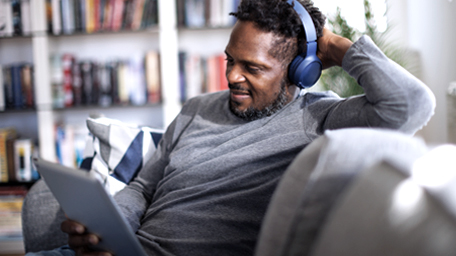 Smiling man with bluetooth headphones watching movie on digital tablet at home