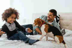 African American Father And Daughter Spending Time Together With A Dog On A Bed